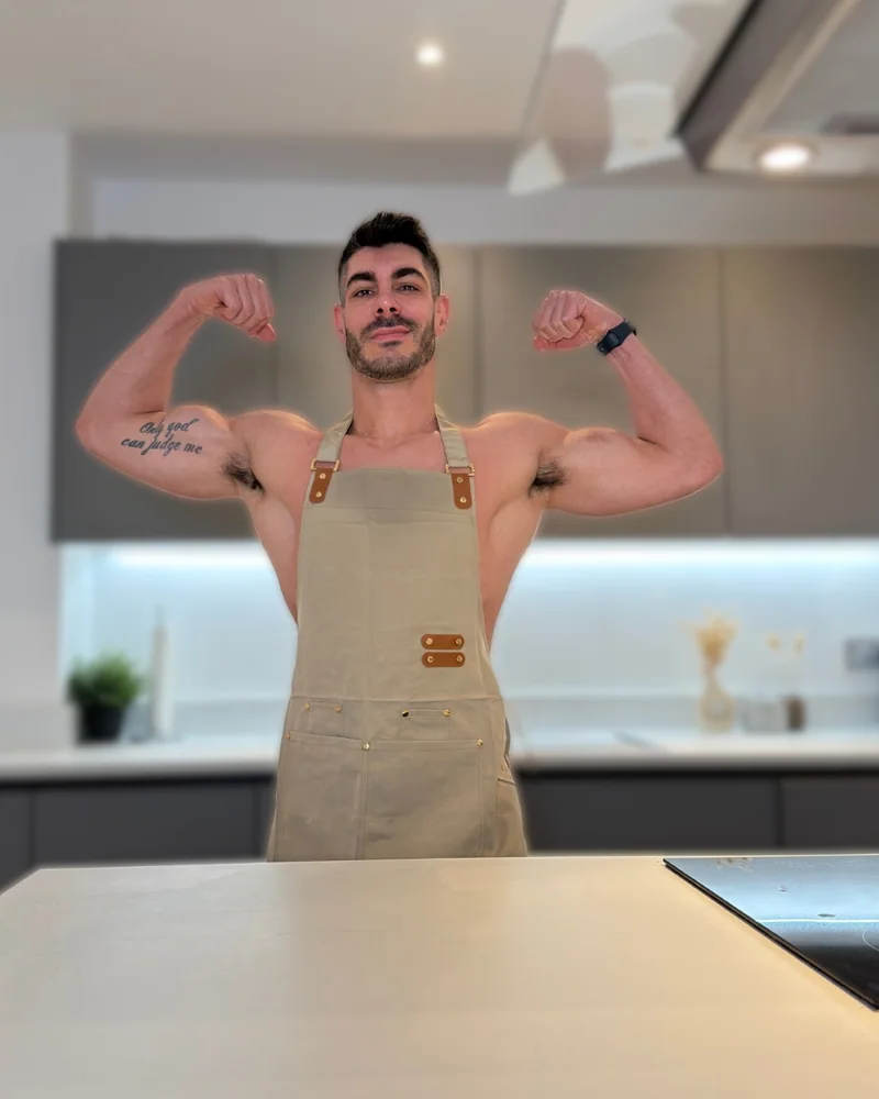 Atai flexing his arms while wearing an apron in his kitchen